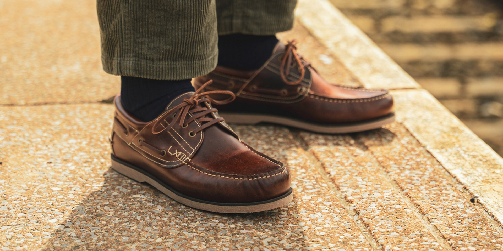 A man sat on a wooden stool, wearing the LANX men's, Brinscall // Tan, moccasin constructed derby shoes.