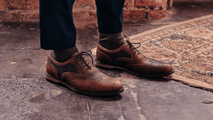 A man wearing the LANX Shireburn Khaki & Brown, oxford brogue shoes. Stood on a concrete floor with a rug.