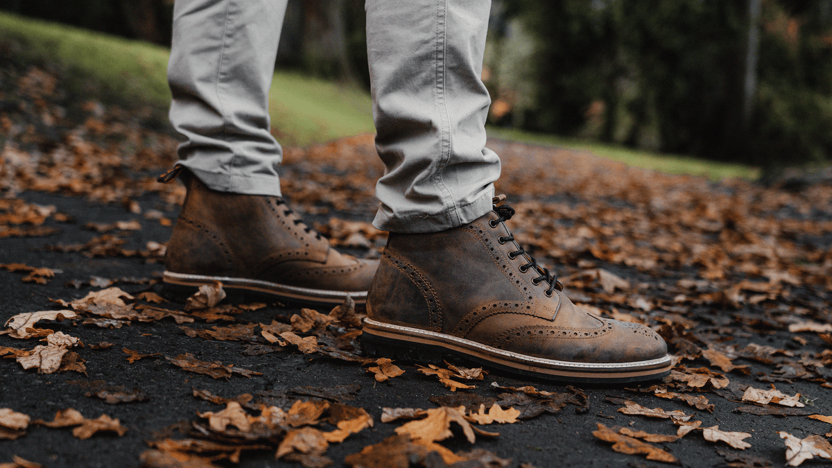 A man stood on a leaf covered, park path, wearing the LANX, men's, Bayley // Rust Distressed, derby brogue boots.
