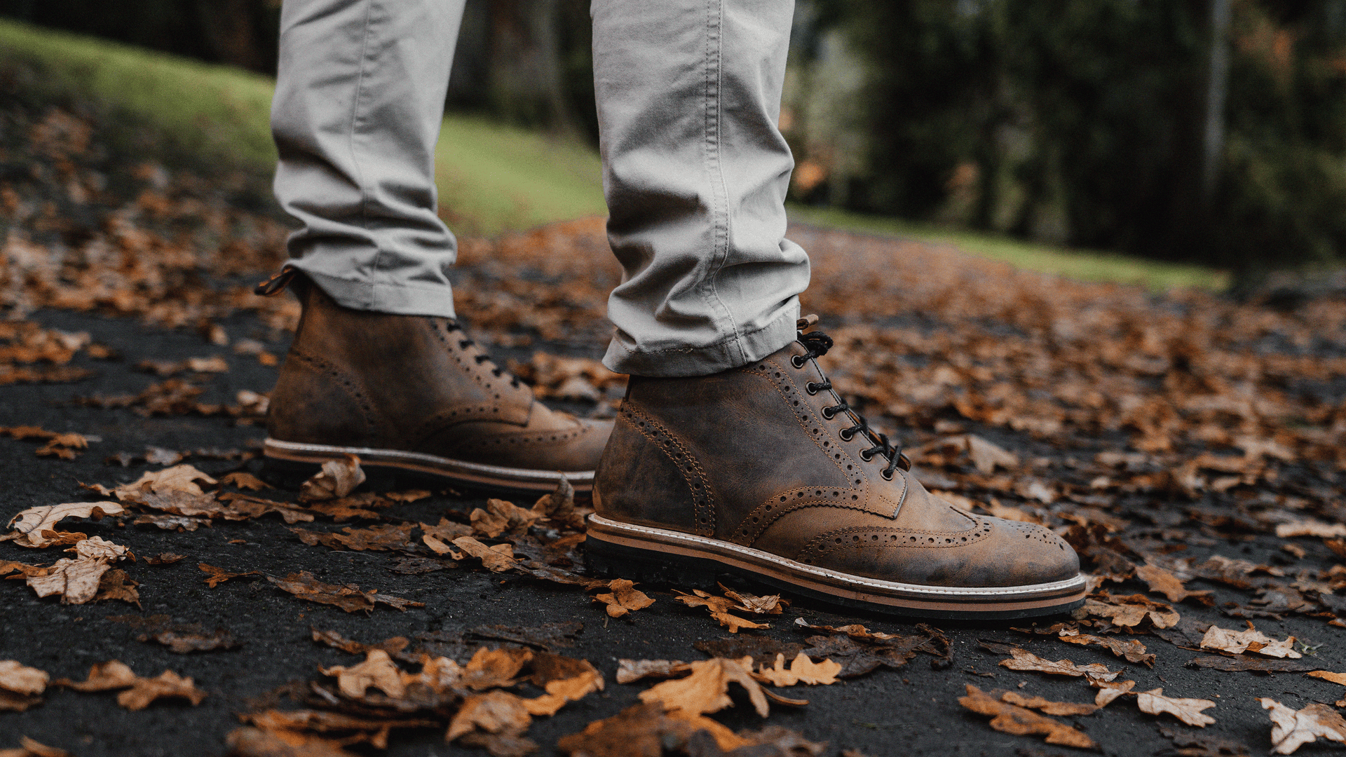 A man stood on a leaf covered, park path, wearing the LANX, men's, Bayley // Rust Distressed, derby brogue boots.