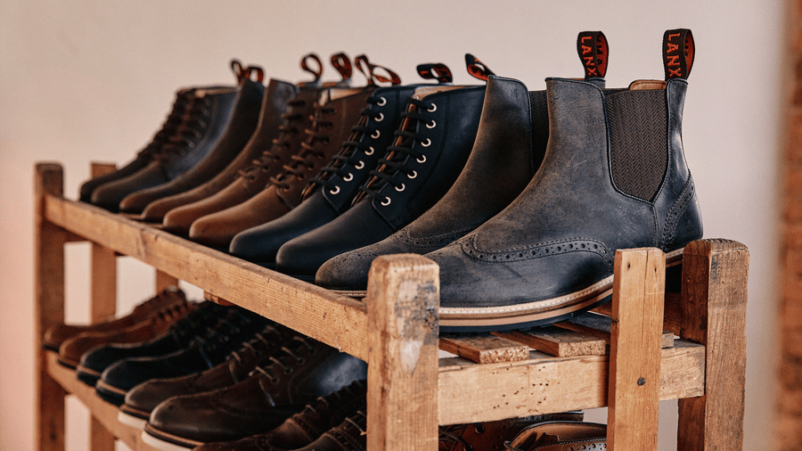 LANX grey, black and brown, derby and chelsea boots on a wooden shoe rack.