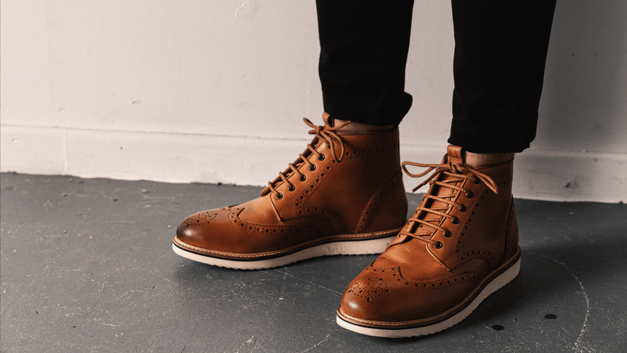 A man's feet wearing the LANX, Newton // Tan, EVA soled, derby brogue boots. Stood on a concrete floor.