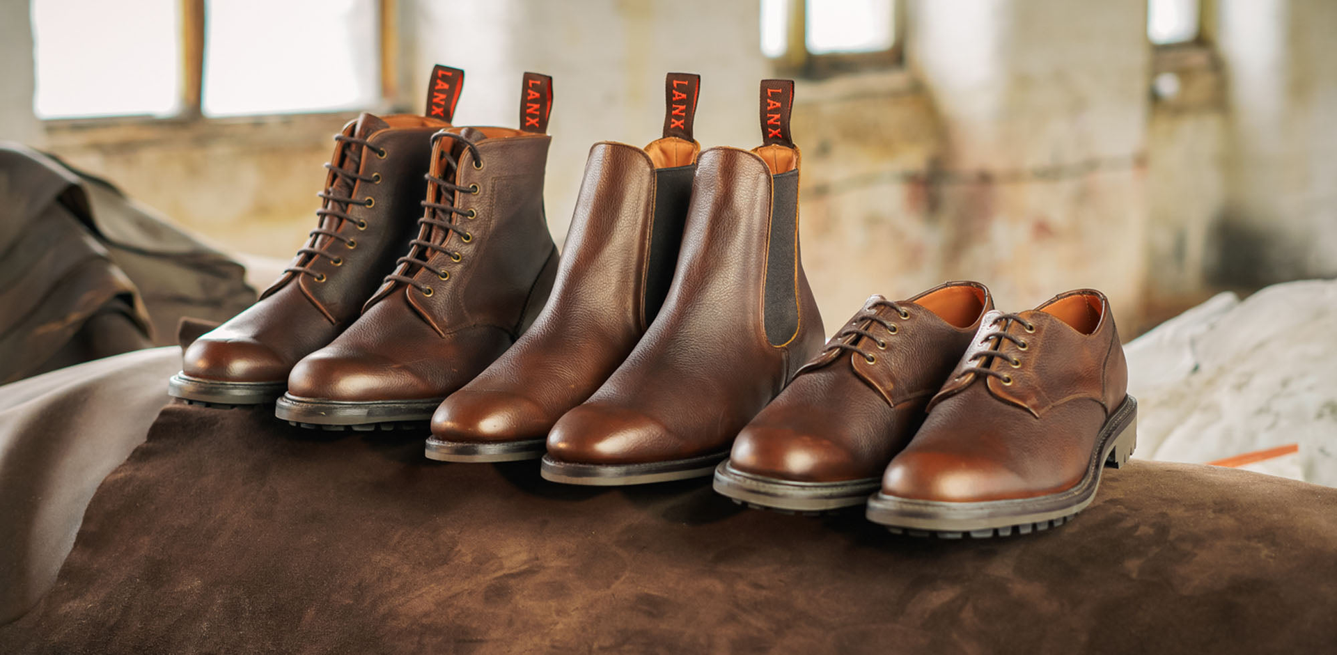 A mixture of LANX, goodyear welted, grey, brown and tan, derby boots and shoes on a wooden shoe rack.