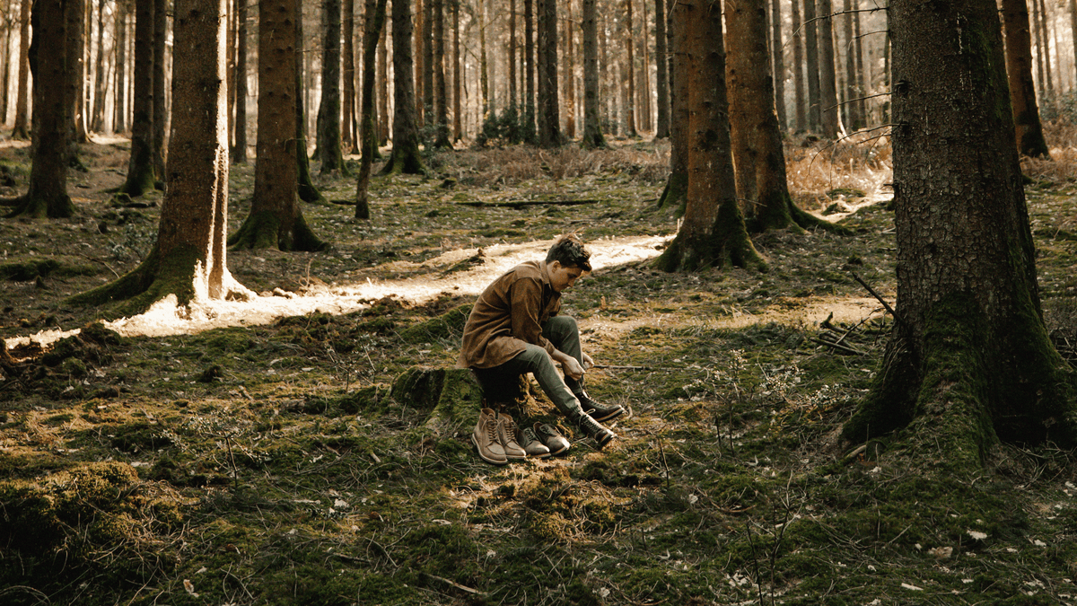 A man sat on a tree stump lacing up the LANX, Bamber Brown Distressed. Rugged, goodyear welted, boots.