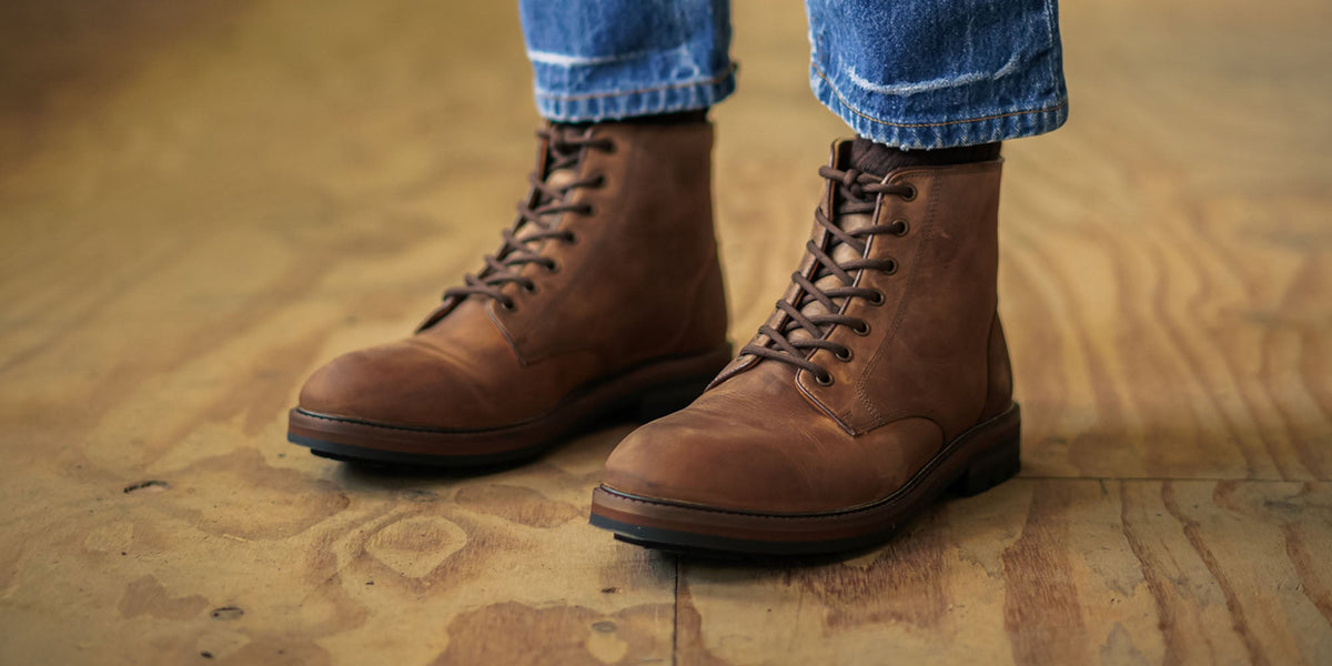 A man wearing the Bayley Auburn, derby boots sat on a wooden chest.