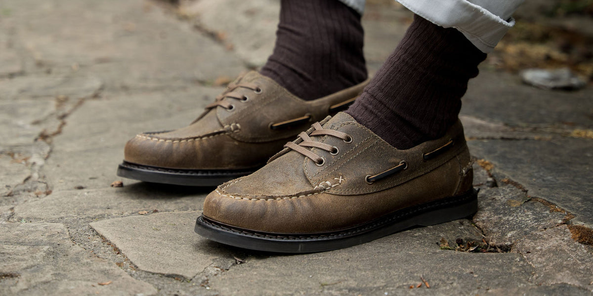 A man sat on a wooden stool, wearing the LANX men's, Brinscall // Tan, moccasin constructed derby shoes.