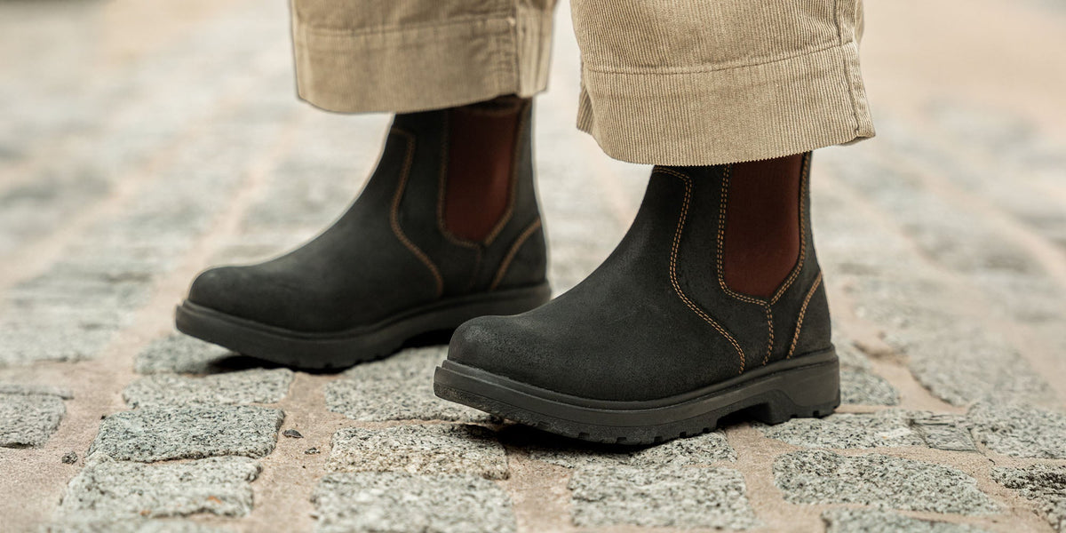 A woman wearing the LANX Whalley Black Grained, lace-to-toe boots. Stood on a conrete floor in a redbrick room.